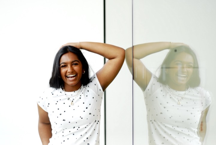 Anya laughing with her arm raised, doubled in a glass wall reflection