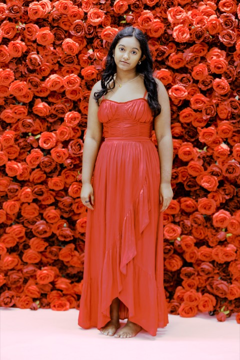 Anya standing in a red gown against the wall of red roses
